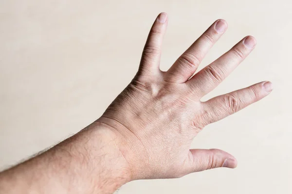 top view of male back of hand with spread out five fingers close up over light brown wooden board