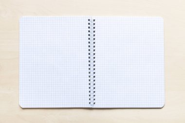 Açık kahverengi tahta üzerinde kare sayfalı boş spiral defter üst görünümü
