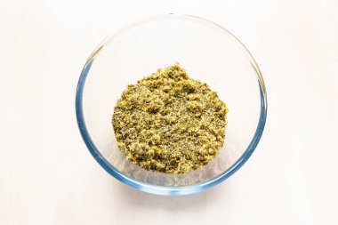 Kurumuş, ezilmiş şifalı bitkilerin ve açık kahverengi masadaki cam kasenin içindeki bitkilerin manzarası.