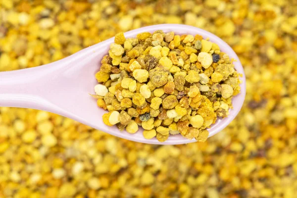 Pembe seramik kaşığın üst görüntüsü ve doğal arı poleni arka planda bulanık arı ekmeğinin üzerine kapanıyor.