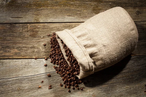 Burlap sack of coffee beans against dark wood background — Stock Photo, Image