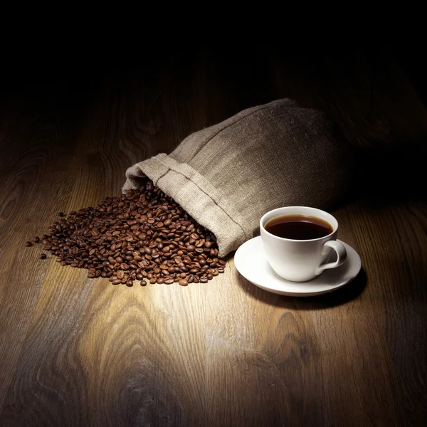 Coffee cup with burlap sack of roasted beans on rustic table Royalty Free Stock Images