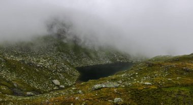 Koyu yeşil dağ gölü, yoğun sis ile yürüyüş yaparken panorama manzarası