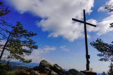 Ağaçlar ve kayaların arasındaki dağda mavi gökyüzünde beyaz bulutlar olan bir zirve.