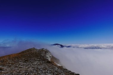 Derin mavi gökyüzü ve yoğun sis bir dağdan zirveye yürürken