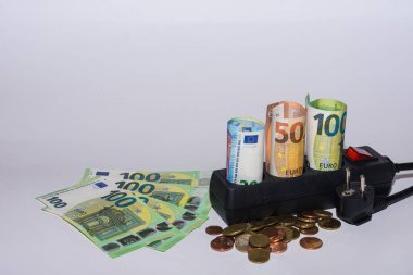 Enerji tüketimi ve elektrik fiyatlarındaki artış. Gri arka plan görünümlü elektrik şeridi olan çok sayıda euro banknot ve sikke.