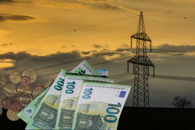 Elektrik direği gün batımında elektrik fiyatlarındaki artışa ilişkin 100 avro fatura ve sikkelerle