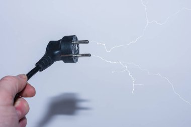 Bir elinde eğimli fişle elektrik tasarrufu ve gri sırtüstü dallanmış bir yıldırım