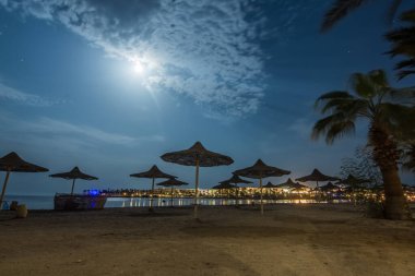 Plaj şemsiyeli kumlu sahil ve Mısır 'da gece parlak bir ay.