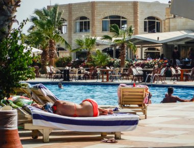 Kırmızı bikinili genç bir kadın havuz kenarında uzanmış, palmiye ağaçları Mısır 'da.