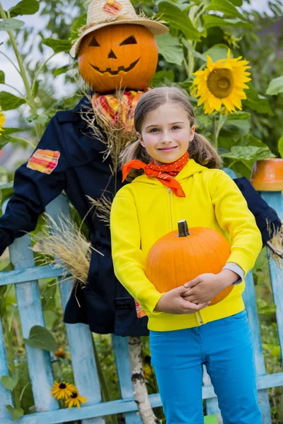 Scarecrow and happy girl  in the garden - Autumn harvests — Stock Photo, Image