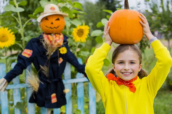 Scarecrow and happy girl  in the garden - Autumn harvests — Stock Photo, Image