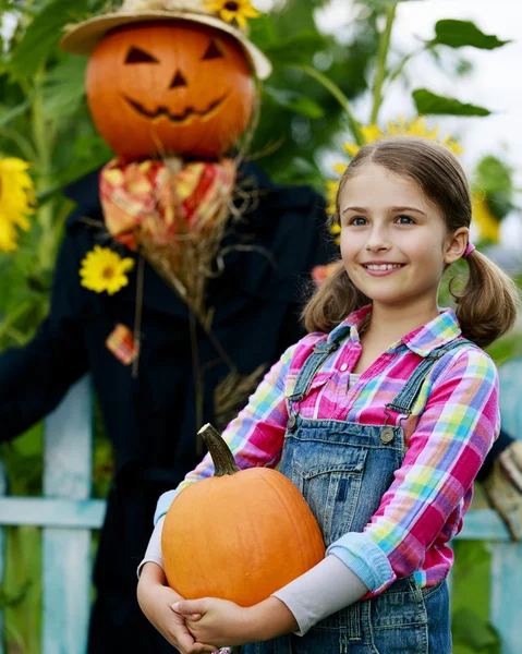 Scarecrow and happy girl  in the garden - Autumn harvests — Stock Photo, Image