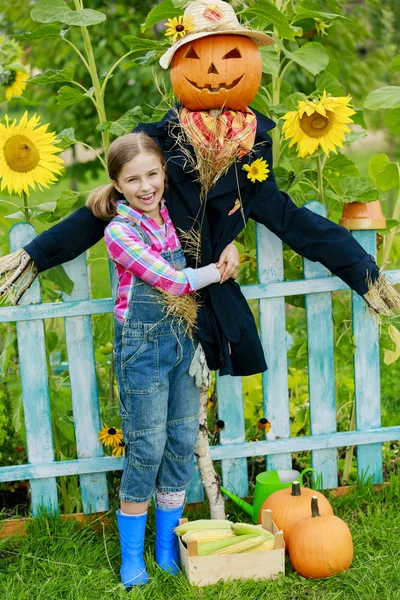 Scarecrow and happy girl  in the garden — Stock Photo, Image