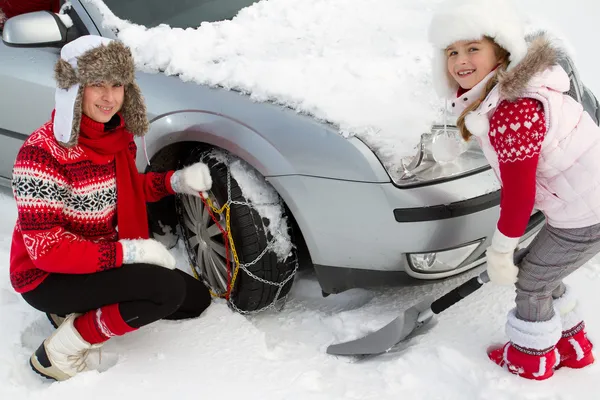 Зима, путешествия - женщина накладывает цепи противоскольжения на шины автомобиля — стоковое фото