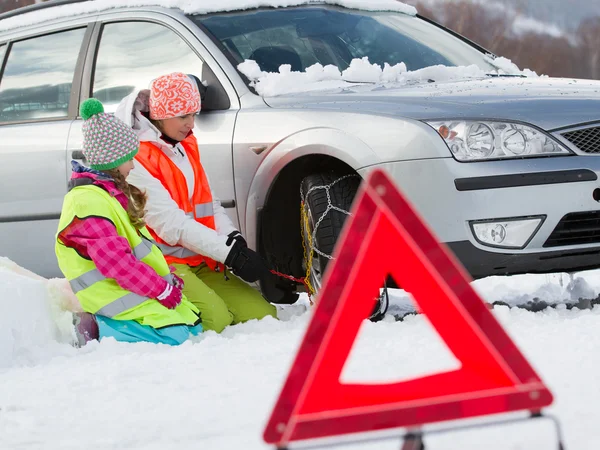 Invierno, viaje - mujer poniendo cadenas de nieve en el neumático del coche —  Fotos de Stock