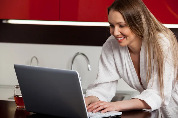 Uśmiechnięta młoda kobieta korzysta z laptopa w kuchni w domu — Zdjęcie stockowe