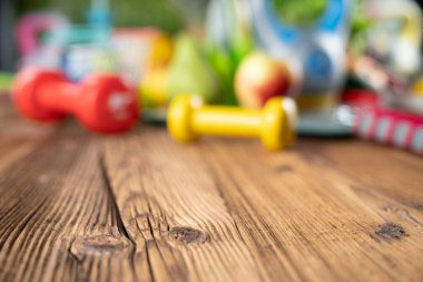 Fitness konsepti. Sağlıklı beslenme: meyve ve sebze. Spor aletleri: tartı makinesi ve ahşap masa üzerindeki dambıllar.