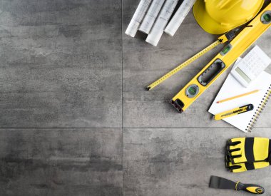 Müteahhit teması. Müteahhidin alet çantası, sarı başlık, libella, el testeresi. Gri fayansların üzerinde planlar ve defter.