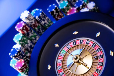 Kumarhane teması. Kumar oyunları. Mavi arka planda rulet ve poker fişleri.