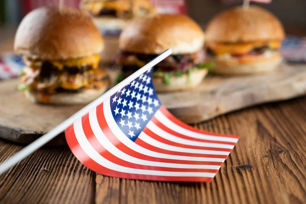 Fourth of July celebration. American flag and decorations. Burgers on rustic wooden table.