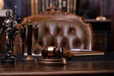 Yargıç ofisi. Heykel ve tokmak yargıç masasının üzerinde. Arkaplanda kitap rafı ve yargıç koltuğu.