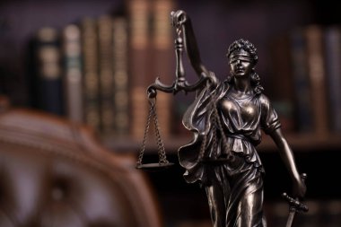 Yargıç ofisi. Heykel ve tokmak yargıç masasının üzerinde. Arkaplanda kitap rafı ve yargıç koltuğu.