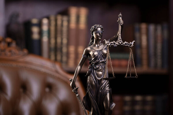 Judge office. Themis sculpture and gavel on the judge desk. Book shelf and judge chair in the background.