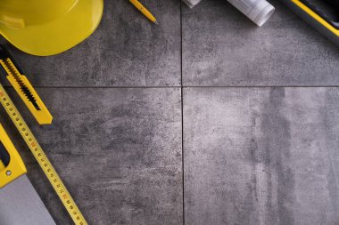 Müteahhit teması. Müteahhidin alet çantası, sarı başlık, libella, el testeresi. Gri fayansların üzerinde planlar ve defter.