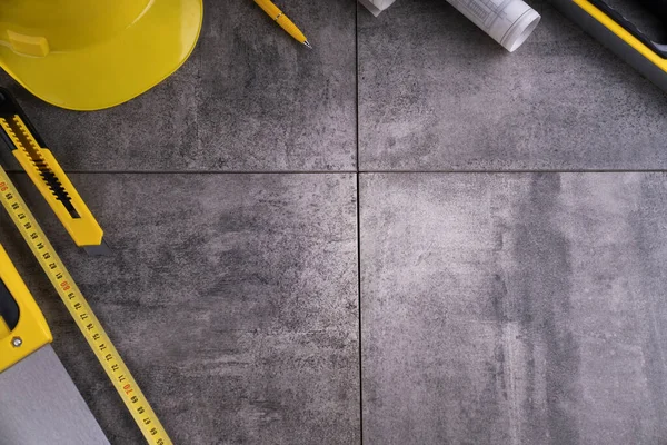 Müteahhit teması. Müteahhidin alet çantası, sarı başlık, libella, el testeresi. Gri fayansların üzerinde planlar ve defter.