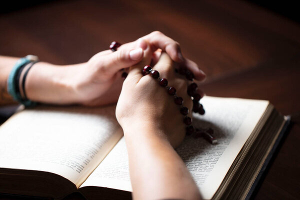 Христианство тема молитвы. Христианка с Библией молится руками, скрестив четки.