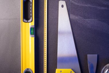 Müteahhit teması. Müteahhitin planları, defter ve alet çantası: sarı baret, iftiracı, gri fayansların arka planında testere ve yarda..