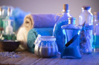 Spa and wellness concept. Bottles with bath and spa cosmetics, rolled up towels, bath salts and care products on wooden rustic paneling.