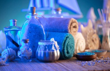 Spa and wellness concept. Bottles with bath and spa cosmetics, rolled up towels, bath salts and care products on wooden rustic paneling.