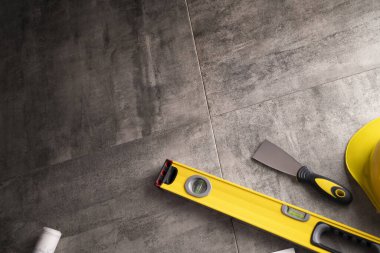 Müteahhit teması. Müteahhitin planları, defter ve alet çantası: sarı baret, iftiracı, gri fayansların arka planında testere ve yarda..