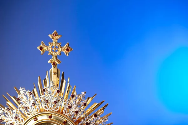 Catholic religion concept. Catholic symbols composition. The Cross, monstrance,  Holy Bible and golden chalice on wooden altar and blue bokeh background.