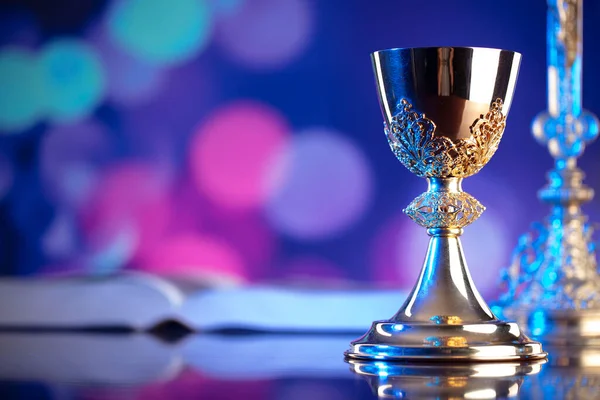 Catholic religion concept. Catholic symbols composition. The Cross, monstrance,  Holy Bible and golden chalice on wooden altar and blue bokeh background.