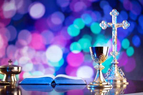 Catholic religion concept. Catholic symbols composition. The Cross, monstrance,  Holy Bible and golden chalice on wooden altar and blue bokeh background.