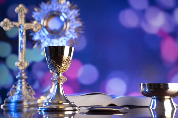 Catholic religion concept. Catholic symbols composition. The Cross, monstrance,  Holy Bible and golden chalice on wooden altar and blue bokeh background.