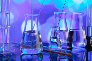 Covid 'e karşı test ve ilaç ile ilgili laboratuvar araştırmaları. Mavi bokeh arka planda cam tüpler ve beherler.