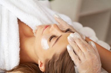 Yüzünde kil maske olan çekici ve komik bir kadın..