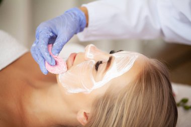 Yüzünde kil maske olan çekici ve komik bir kadın..