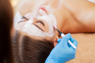 Yüzünde kil kaplıca maskesi olan çekici, komik bir kadın..