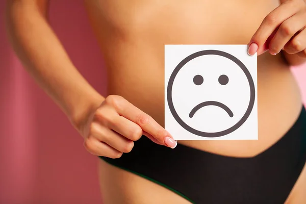 Salud de la mujer, cuerpo femenino sosteniendo triste sonrisa tarjeta cerca del estómago. — Foto de Stock