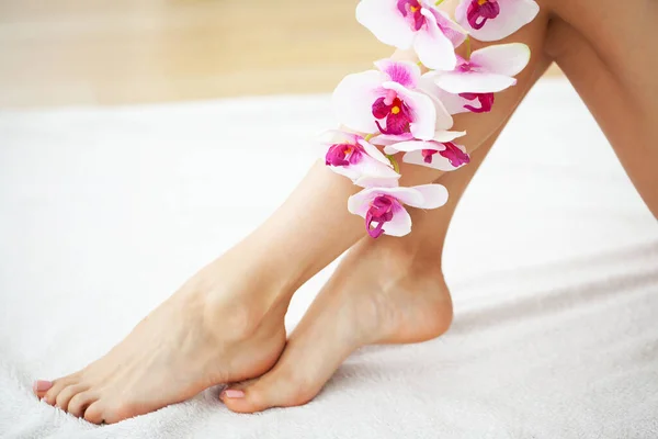 Las piernas largas de una mujer con una manicura fresca y flores de orquídea — Foto de Stock