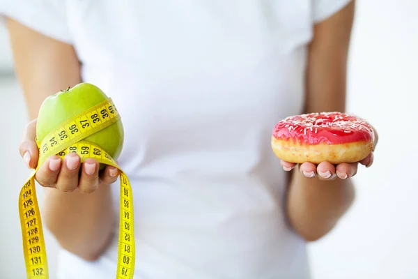 Jeune fille attrayante fait le choix entre la nourriture saine et nocive tenant pomme et un hamburger dans ses mains. — Photo