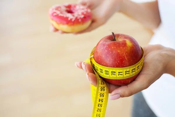 Giovane ragazza attraente sta facendo la scelta tra cibo sano e dannoso tenendo mela e un hamburger nelle sue mani. — Foto Stock