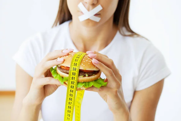 Концепция диеты женщина с запечатанным ртом держит жирный бургер — стоковое фото