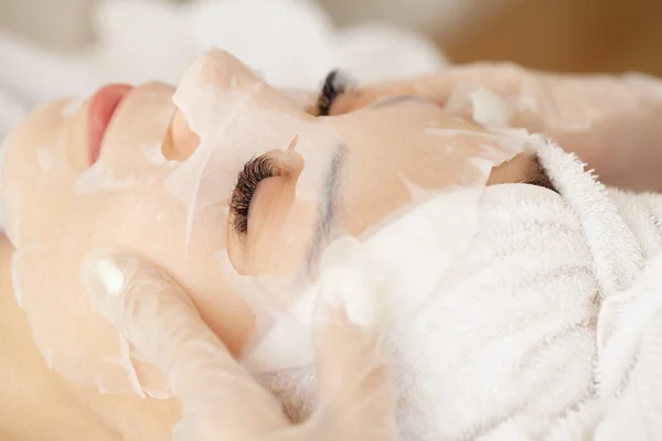 Mulher bonita está aplicando uma máscara de tecido cosmético em um rosto — Fotografia de Stock