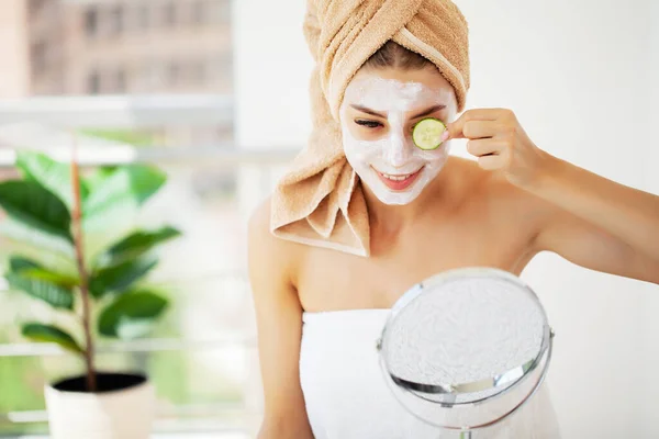 Mulher aplicando máscara em seu rosto e olhando no espelho . — Fotografia de Stock